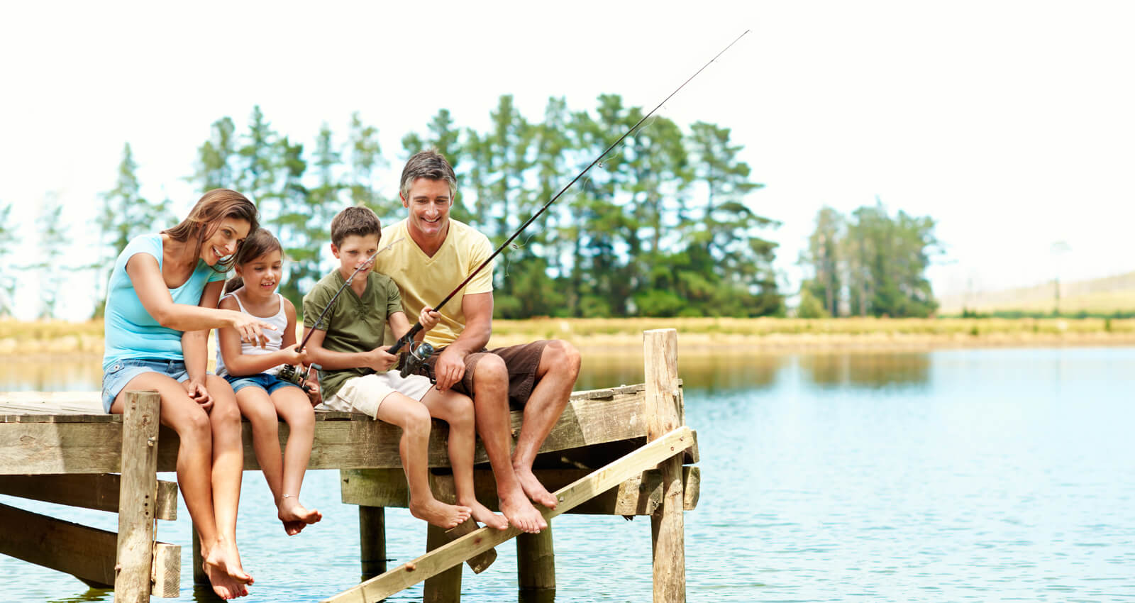 a family of four fishing from a wooden dock by a lake