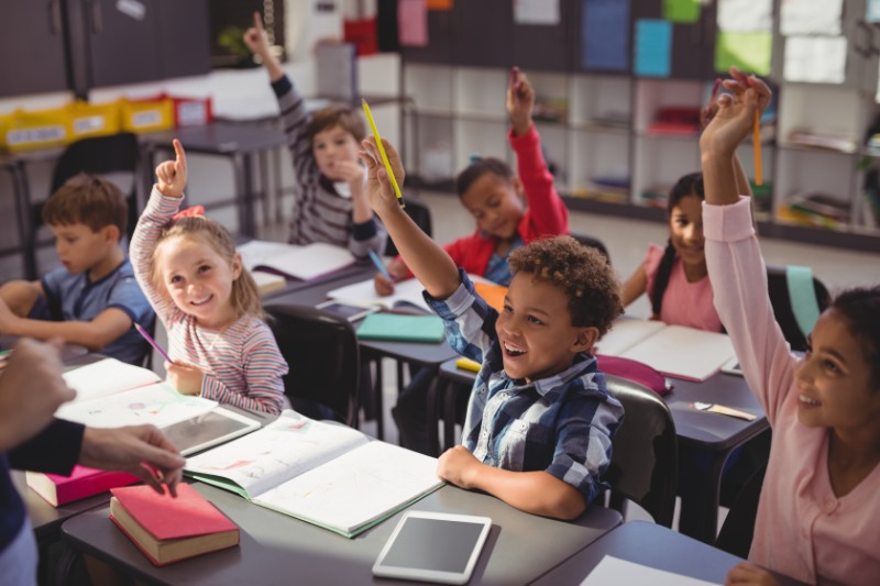 Schoolkids raising their hands in classroom 
